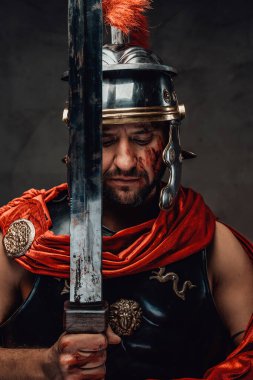 Kara arka planda kılıçla poz veren ciddi Romalı savaşçı.