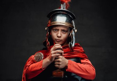 Karanlık arka planda kırmızı pelerinli neşeli Romalı çocuk.