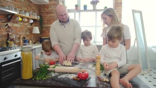 Loving happy young parents teaching cute three sons learning of kneading dough. — Stock Video