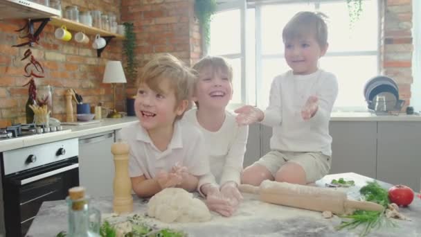 Τρεις Καυκάσιοι χαμογελαστοί αδελφοί παίζουν με αλεύρι στην κουζίνα. — Αρχείο Βίντεο