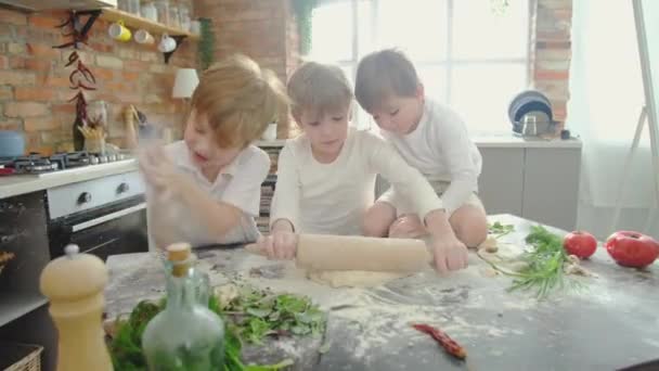 Drei kleine Kinder mit blonden Haaren backen Pizza und rollen den Teig in der Küche. — Stockvideo
