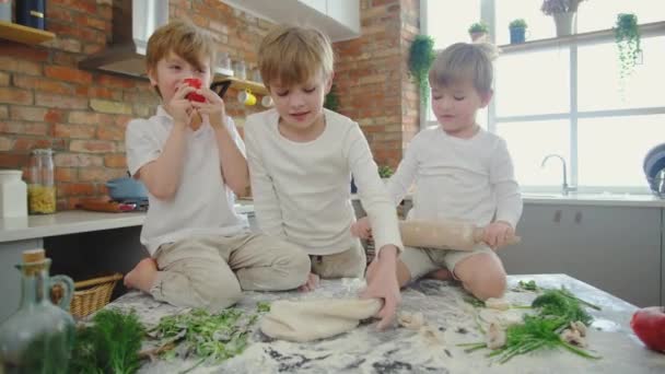 Großaufnahme kaukasische Jungen rollen Teig mit Nudelholz, während sie auf dem Tisch sitzen. — Stockvideo