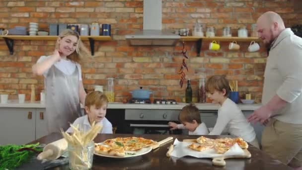 Una gran familia hambrienta de tres chicos está corriendo a la mesa de la cocina donde hay pizza. — Vídeos de Stock