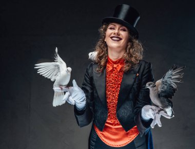Karanlık stüdyoda silindir şapka takan neşeli bir aktris ve küçük beyaz kuşlar.