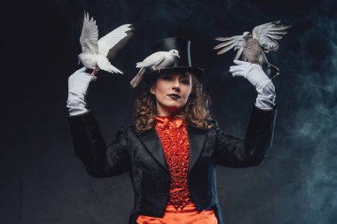 Dumanlı arka planda eğitimli beyaz güvercinleri olan çekici bir kadın oyuncu.