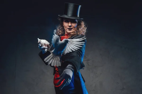 Serious female magician with white pigeons and top hat in dark background — Stock Photo, Image