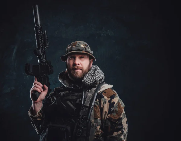 Komoly fickó álcázó jelmezben, kezében egy puskával sötét háttérben. — Stock Fotó
