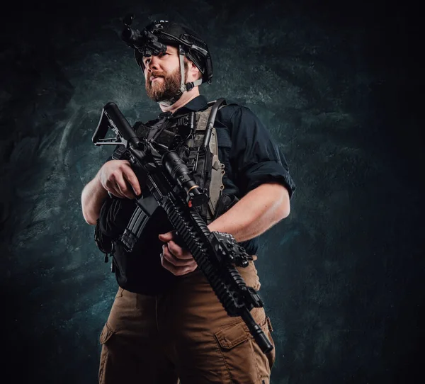 Soldado com capacete e colete fica segurando um rifle no fundo escuro — Fotografia de Stock