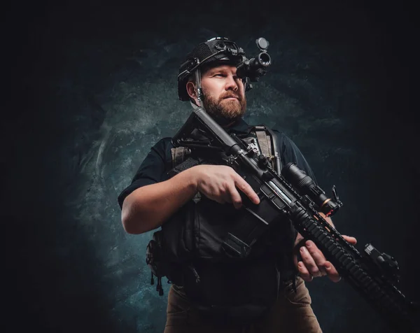 Martial guy kijkt in nachtzicht apparaat houdt zijn geweer in donkere achtergrond — Stockfoto