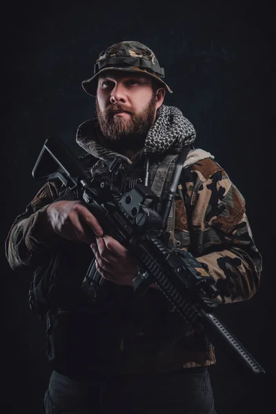 Chico serio con disfraz de camuflaje sosteniendo un rifle en fondo oscuro — Foto de Stock