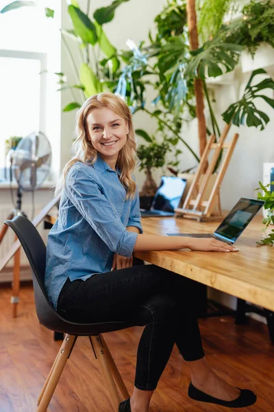 Trabalhadora de escritório atraente e feliz se senta à mesa com um laptop — Fotografia de Stock