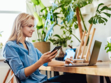 Ofisinde akıllı telefonu ve bilgisayarı olan genç bir ofis çalışanı.