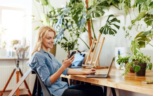 Jovem trabalhadora de escritório com um smartphone e laptop no escritório — Fotografia de Stock