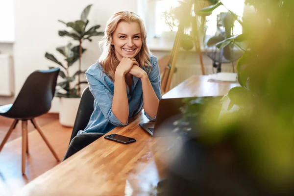 Joyeuse jeune femme pose dans la salle de bureau avec ordinateur portable à la table — Photo