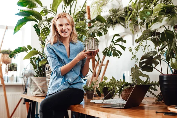 Retrato de uma jovem mulher cuidadosa com planta de sala sentada na mesa — Fotografia de Stock