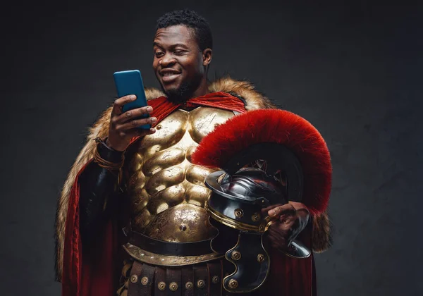 Gioioso uomo nero in costume da soldato romano con smartphone — Foto Stock
