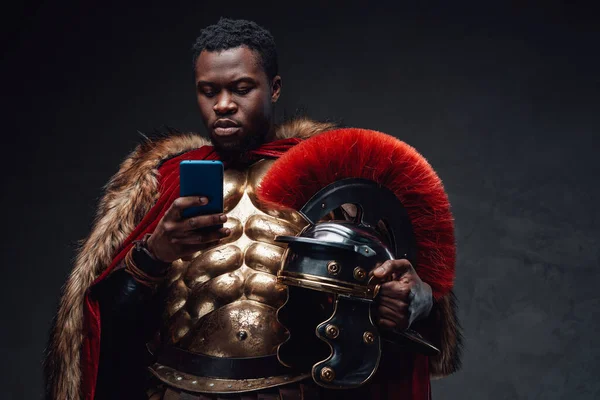 Homem negro em trajes de soldado romano usando smartphone — Fotografia de Stock