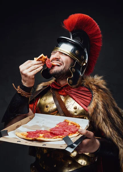 Antyczny legionista je pizzę na ciemnym tle. — Zdjęcie stockowe