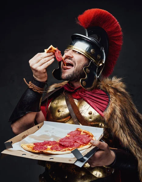 Antique legionary eats pizza against dark background — Stock Photo, Image