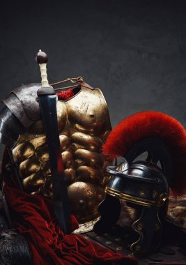 Kasklı ve kılıçlı zırhlı, karanlık arka planda.