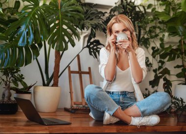 Kahve fincanı ve dizüstü bilgisayarı olan neşeli genç bir kadın.