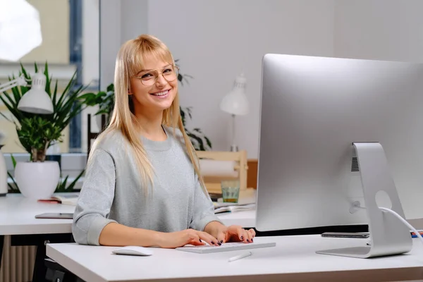 Zufriedene Geschäftsfrau sitzt am Tisch und blickt im Büro in die Kamera — Stockfoto