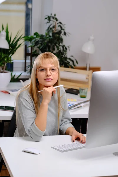 Geschäftsfrau mit Brille sitzt im Büro am Tisch und blickt in die Kamera — Stockfoto