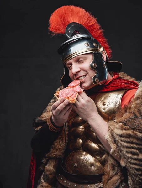 Радостный легионер в бронзовых доспехах ест пиццу — стоковое фото