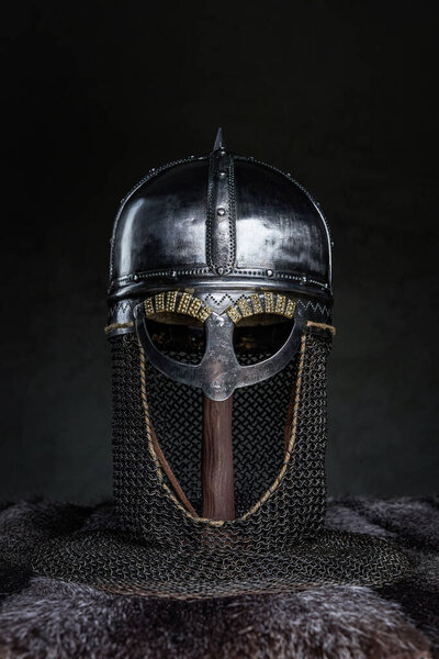 Medieval single helmet with chain mail and fur against dark background.