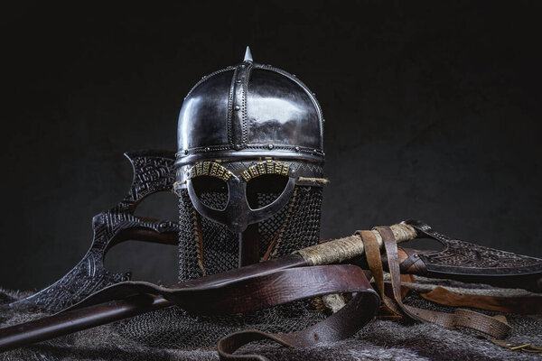 Isolated in dark background knight iron helmet around axes belt and fur.