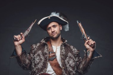 Karanlık arka planda tabancaları olan üzgün bir korsan.