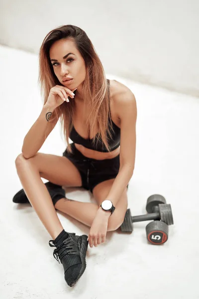 Fitness woman sits on floor around dumbells — Stock Photo, Image