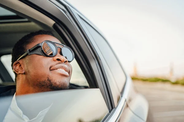 Radosny afrykański biznesmen w okrągłych okularach przeciwsłonecznych w samochodzie — Zdjęcie stockowe