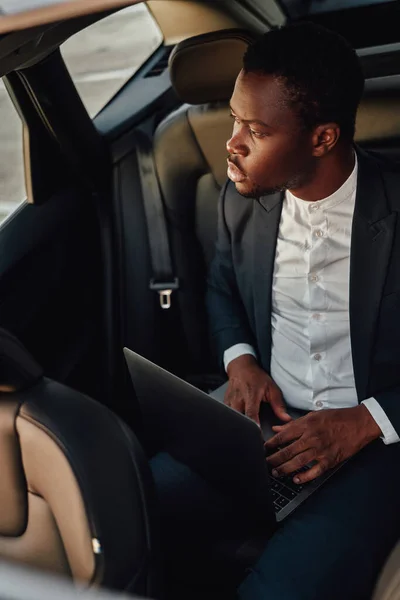 Serious black employee working on laptop inside of car — Stock Photo, Image