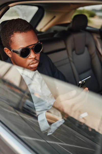 Fajny afrykański biznesmen z telefonem siedzącym w samochodzie — Zdjęcie stockowe