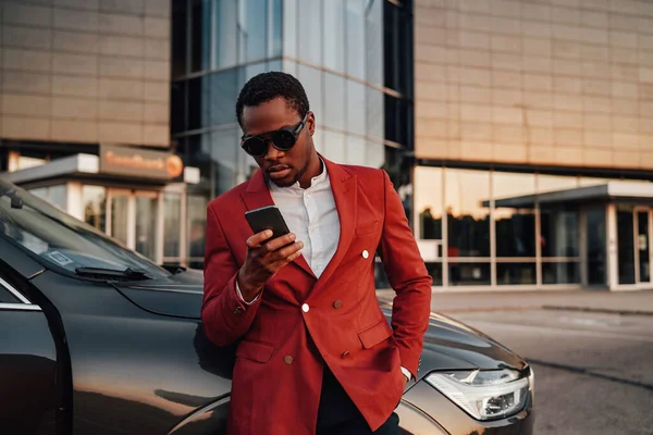 Крутой африканский бизнесмен с телефоном, позирующим вокруг его машины — стоковое фото