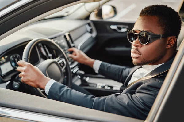 Stylish black businessman inside of car holding wheel — Stock Photo, Image