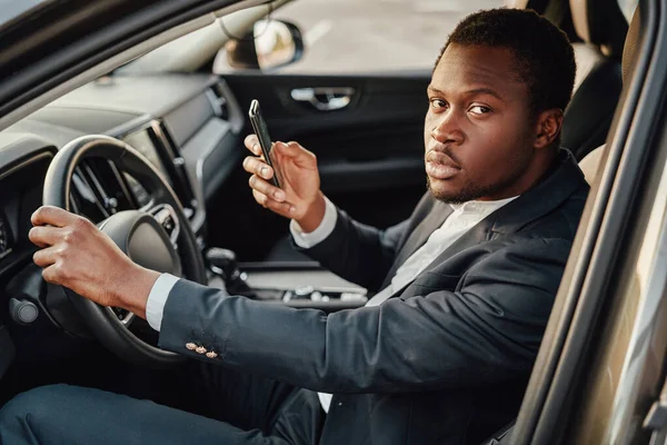 Empresário africano sentado dentro do carro com smartphone — Fotografia de Stock