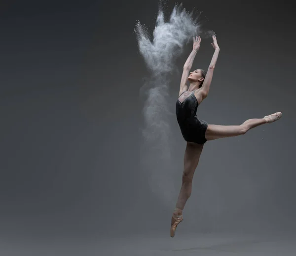Кваліфікована балерина танцює, стрибаючи на сірому фоні — стокове фото