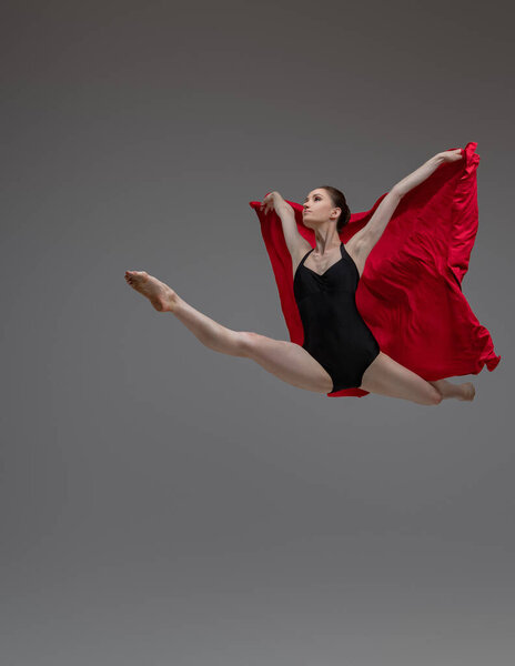Studio shot of jumping ballerina dancer dressed in tutu holding red silk.
