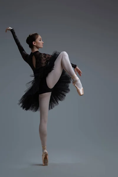 Гнучка балерина в чорній сукні на сірому фоні — стокове фото