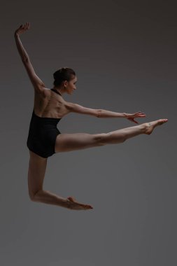 Gri arka planda zıplayan balerinin yan görüntüsü