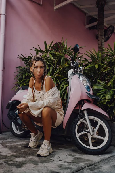 Aantrekkelijke vrouw met scooter rond roze gebouw — Stockfoto