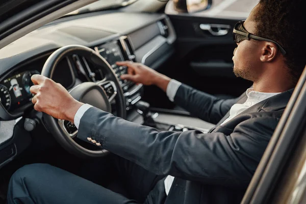 Stylish black businessman inside of car holding wheel — Stock Photo, Image