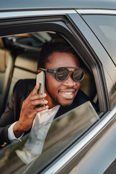 Uśmiechnięty czarny biznesmen ze smartfonem w samochodzie — Zdjęcie stockowe