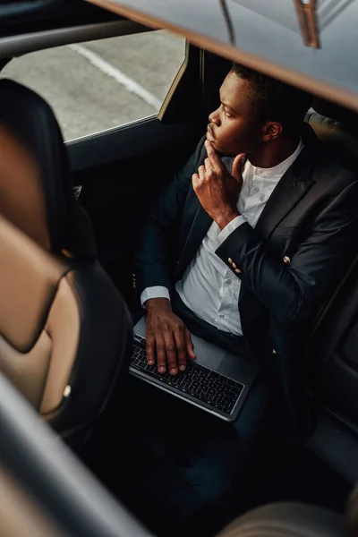 Pensive black employee working on laptop inside of car — Stock Photo, Image