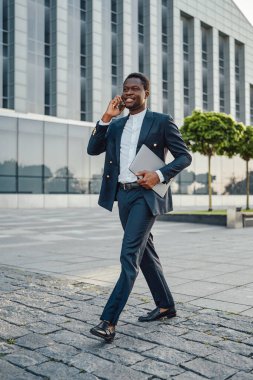 Bilgisayarlı başarılı bir iş adamı dışarıda telefonla konuşuyor.