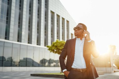Afrikalı iş adamı şehir manzarasına karşı telefonda konuşuyor.