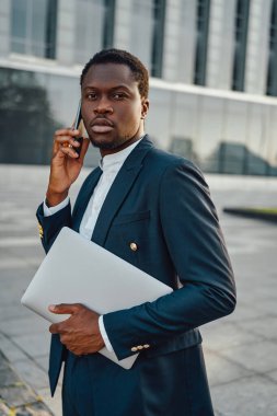 Ciddi bir iş adamı laptopuyla dışarıda telefonla konuşuyor.