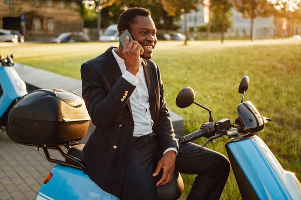 Gioioso impiegato nero in tuta con telefono e scooter — Foto Stock